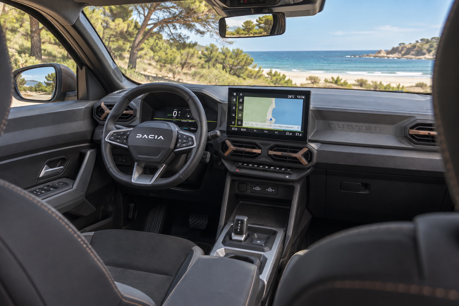 Dacia Duster III interiør set mellem forsæderne med tændte skærme og venstrestyret cockpit